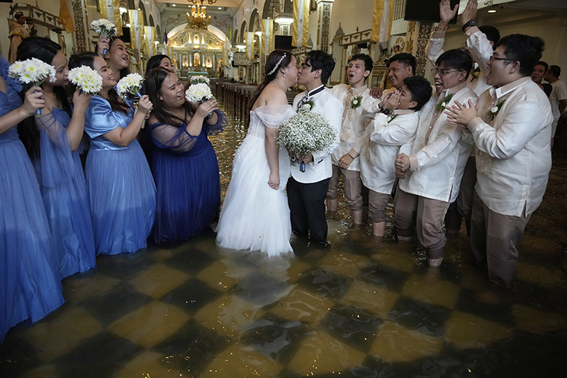 Title: Wedding in the FloodCredit: &copy; Aaron Favila, Associated PressCaption: The newlyweds share a kiss as guests cheer. The couple have been together for ten years. According to Verdillo, &ldquo;This is just one of the struggles that we&rsquo;ve overcome.&rdquo; Malolos, Bulacan province, Philippines, 22 July 2025.Story: When Typhoon Wipha hit the Philippines and flooded Barasoain Church, Jade Rick Verdillo and Jamaica Aguilar faced a difficult decision: should they cancel their wedding or proceed with the marriage? The couple carried on despite high waters, a testament to love and resilience in the face of severe weather. Located on a delta, Bulacan province is vulnerable to more frequent and extreme floods caused by aging drainage systems, dredging projects, overextraction of groundwater, and climate change.
